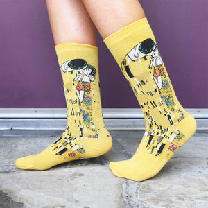 Lifestyle shot of Klimt's The Kiss socks on a person's feet against a purple background.