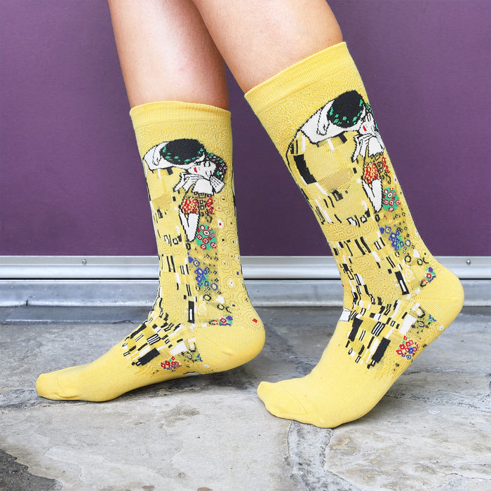 Lifestyle shot of Klimt's The Kiss socks on a person's feet against a purple background.