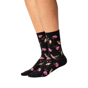 A pair of black socks with a pattern of pink and green hummingbirds and flowers.