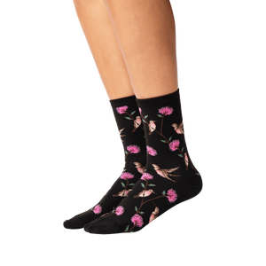 Lifestyle shot of woman's legs wearing black crew socks with hummingbird pattern.