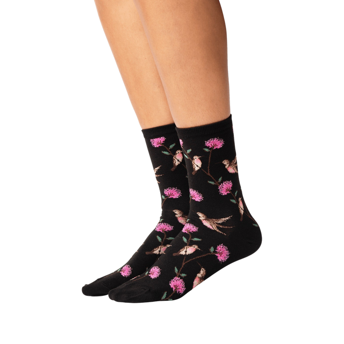 A pair of black socks with a pattern of pink and green hummingbirds and flowers.