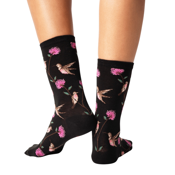 Back view of a pair of black crew socks with a hummingbird and flower pattern.