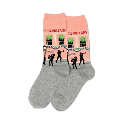 Pair of crew socks. Peach-pink with grey cuffs, they feature a repeating design of a New Orleans street scene with jazz musicians and palm trees.