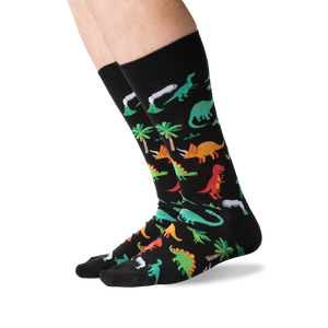 Lifestyle shot showing the dinosaur socks on a person's legs against a green background.
