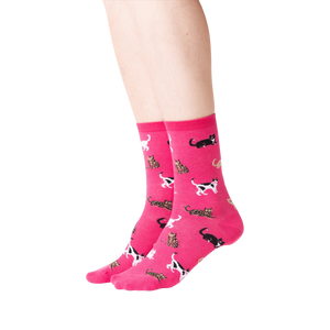 Lifestyle shot showing a person wearing a pair of pink Classic Cats socks. The socks are crew length and feature a pattern of various cats in black, brown, and white.