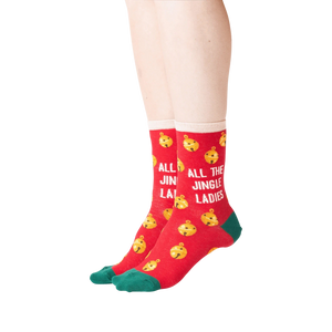 Lifestyle shot showing the socks on a person's feet. The socks are red with gold jingle bells and green cuffs.