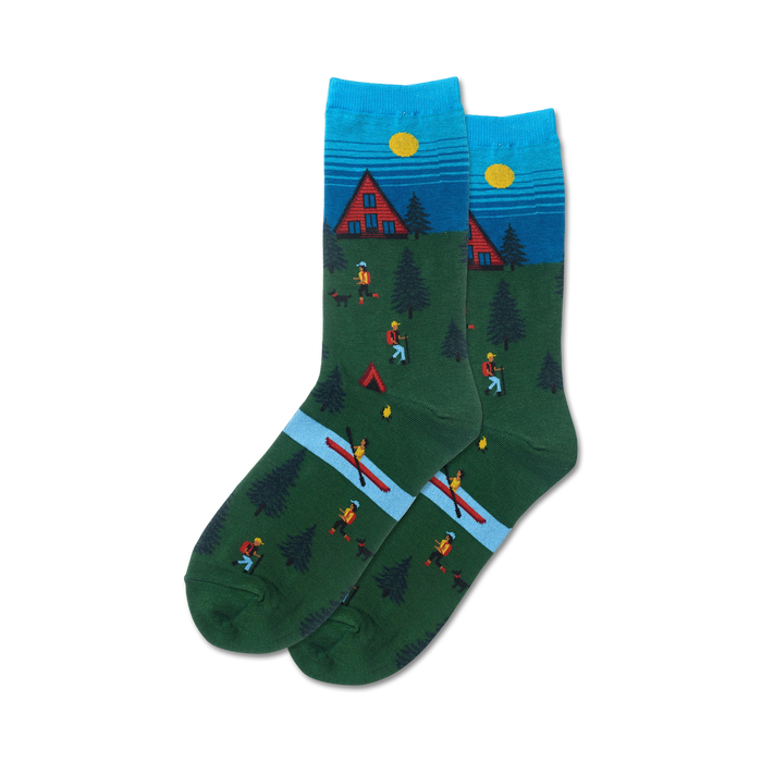 green crew socks with blue and brown accents feature a winter cabin scene with trees, river, canoe, hikers, and a fisher.     }}