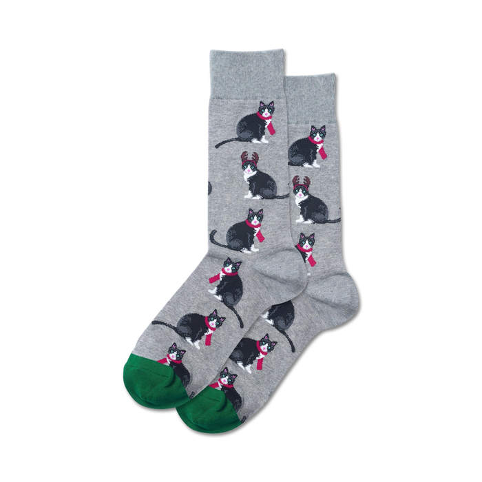 Pair of crew socks; gray background with repeating pattern of black tuxedo cats wearing red scarves and reindeer antlers; green cuffs.