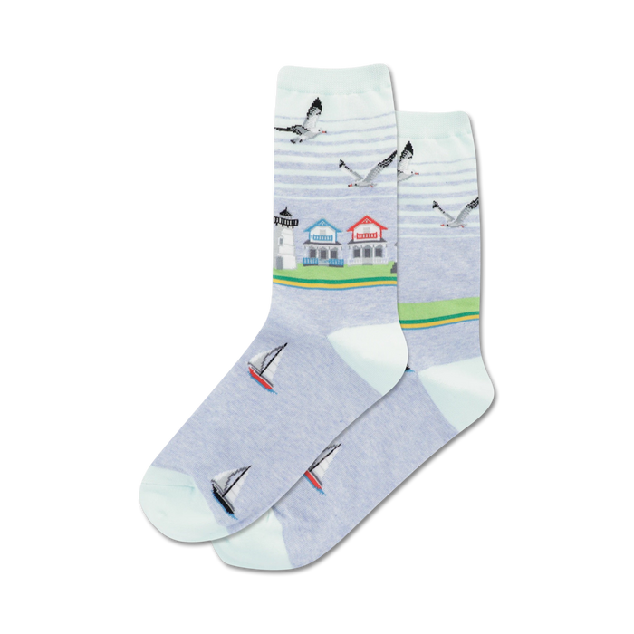 Pair of crew socks in light blue featuring a beach scene: lighthouse, houses, sailboats, and seagulls. }}