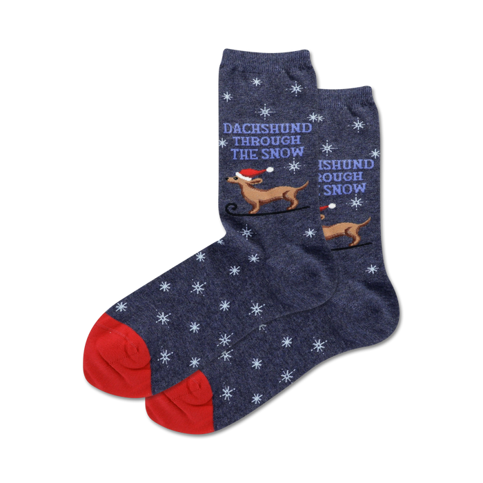 A pair of navy blue crew socks with a red cuff.  They feature a repeating snowflake pattern and illustrations of dachshunds in Santa hats sledding through the snow. }}