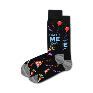 A pair of crew socks in black with a fun 'Happy Me Day' design, featuring colorful party hats, balloons, and streamers.