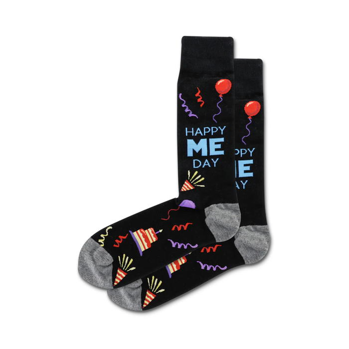 A pair of crew socks in black with a fun 'Happy Me Day' design, featuring colorful party hats, balloons, and streamers.