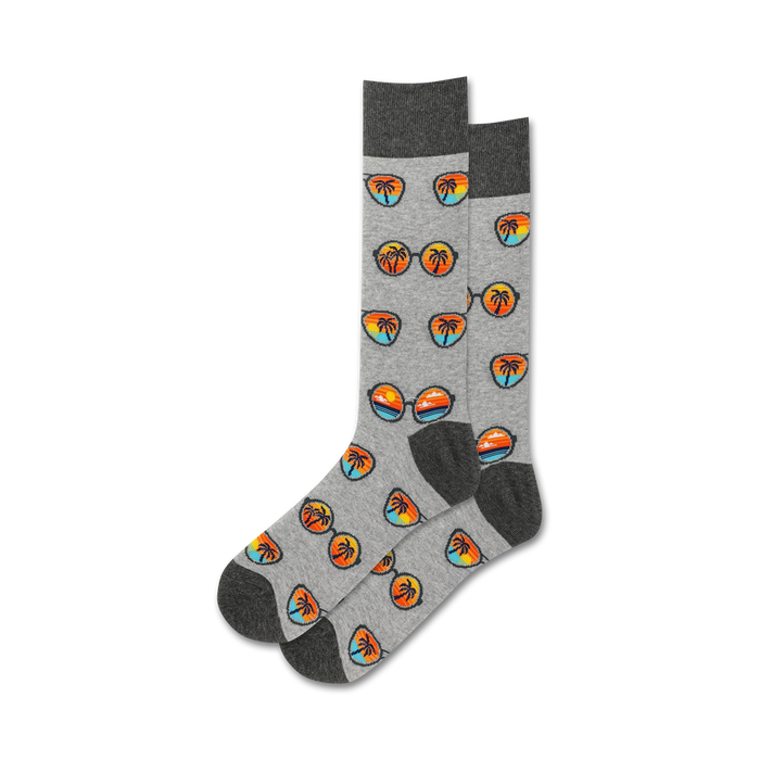 Pair of grey crew socks with a repeating pattern of retro sunglasses and palm trees at sunset. Orange, blue, and black design elements on a heather grey background.