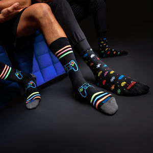 Lifestyle shot of three people wearing different pairs of Hotsox, including the Neon Gamer socks, sitting on blue furniture.