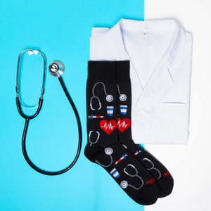 Flat lay of black medical themed socks, a stethoscope, and a folded white lab coat on a blue and white background.