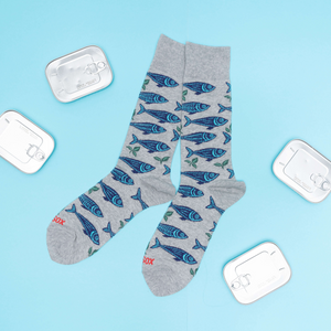 Grey sardine patterned crew socks laid flat on a blue surface, surrounded by four silver empty sardine cans.