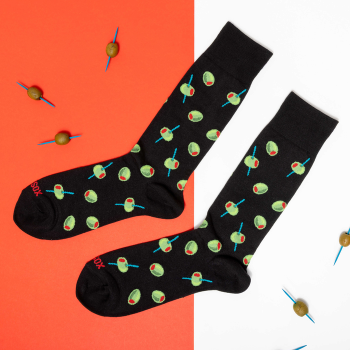 Two black olive pattern socks laid flat on a split orange and white background, with loose olives scattered around.