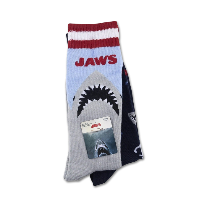 A pair of Jaws socks folded with the packaging. The socks are blue and gray with a red stripe at the top and feature the Jaws logo and a great white shark.