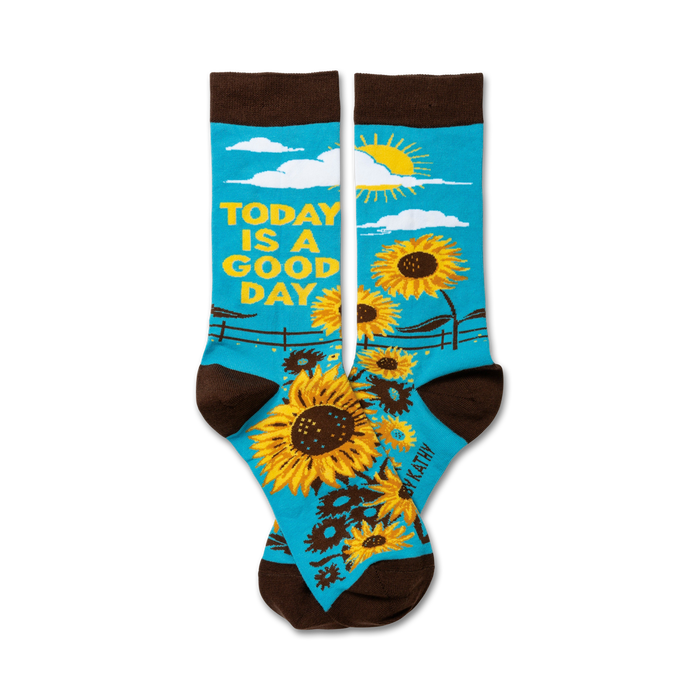 Pair of crew socks. Teal background with sunflowers, a sun, and the text 'Today is a good day'. Brown cuff. }}