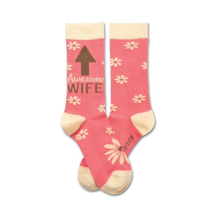 Pair of pink crew socks with a cream cuff. Features a brown arrow pointing up and the words 'Awesome Wife' and a scattered daisy pattern. }}