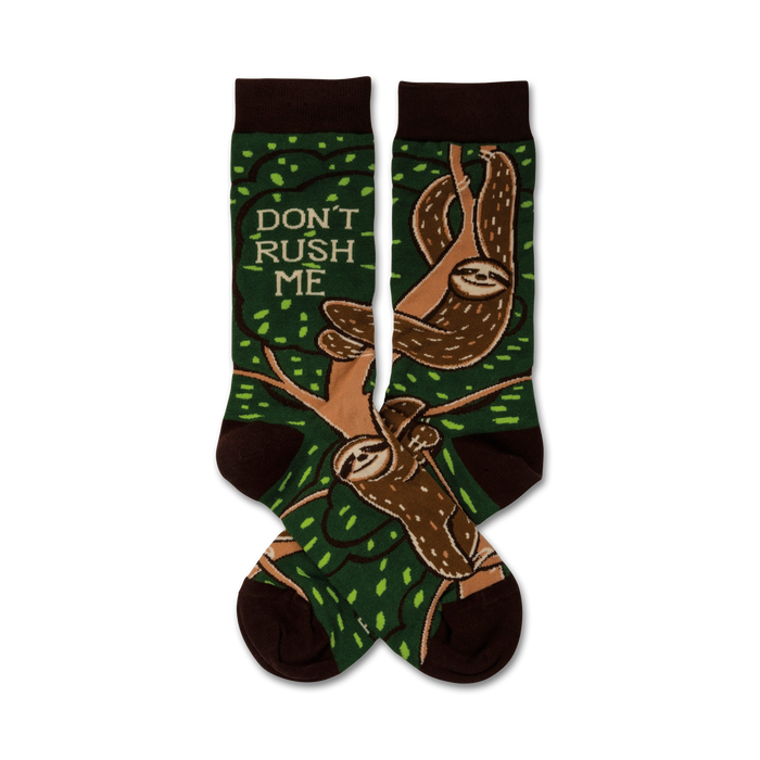 A pair of crew socks with sloths hanging from tree branches on a green background.  The socks are brown and green, and feature the text 'Don't Rush Me'. }}
