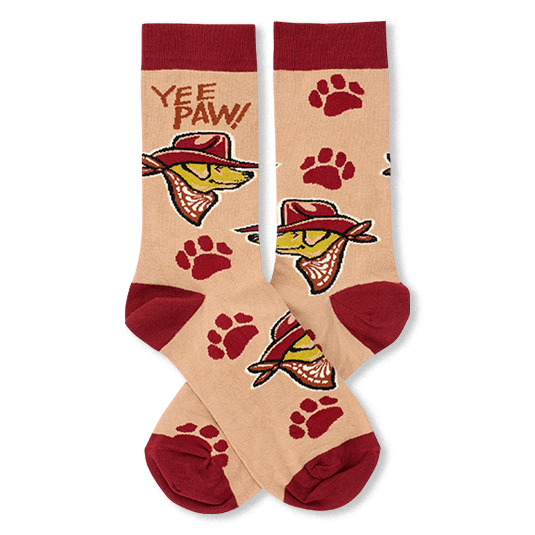 A pair of crew socks with a beige background, featuring a cartoon dog wearing a cowboy hat, red paw prints, and the text 'YEE PAW!' on the upper leg. The socks have solid red cuffs, heels, and toes.