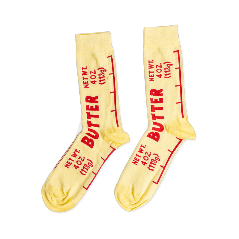 A pair of light yellow ankle socks printed with 'BUTTER' and 'NET WT. 4 OZ. (113g)' in red text, mimicking a stick of butter wrapper.