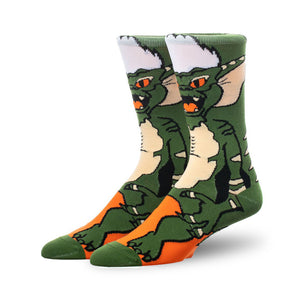 A pair of green and orange crew socks featuring a Gremlin character design. The socks are shown from the side, highlighting the character's face and body.