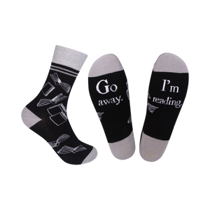 A pair of black crew socks with a grey cuff. The socks feature a white design of open books and the phrases 'Go Away' and 'I'm Reading'.