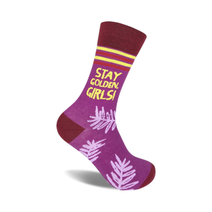 Purple crew socks with maroon cuffs, yellow text reading 'Stay Golden, Girls!', and a light purple leaf pattern.