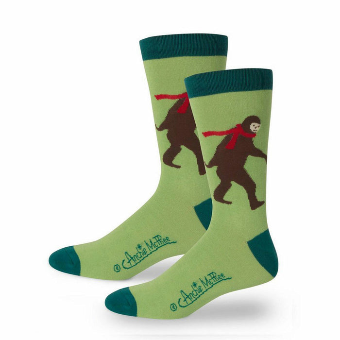 Pair of crew socks featuring a light green background, teal cuffs, and a brown Bigfoot wearing a red scarf. }}