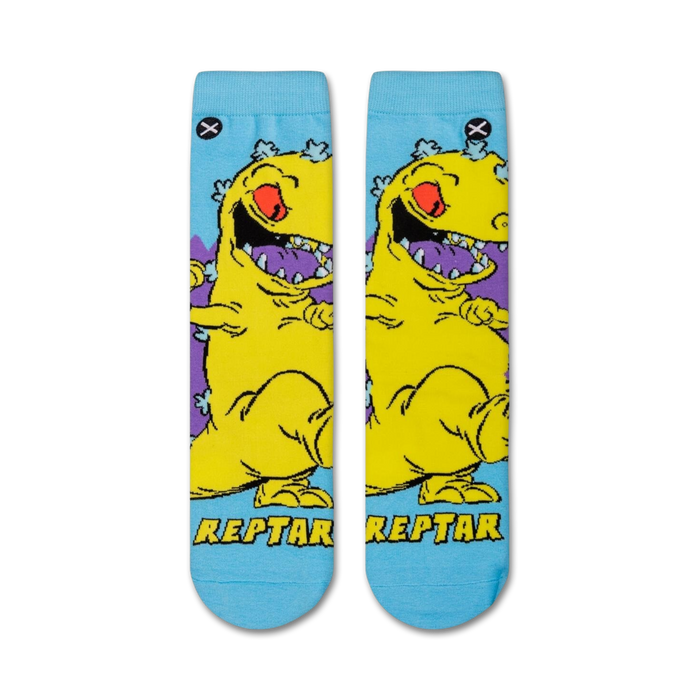 Flat lay showcasing a pair of Rugrats Reptar crew socks. The socks feature a light blue background with a yellow Reptar design.