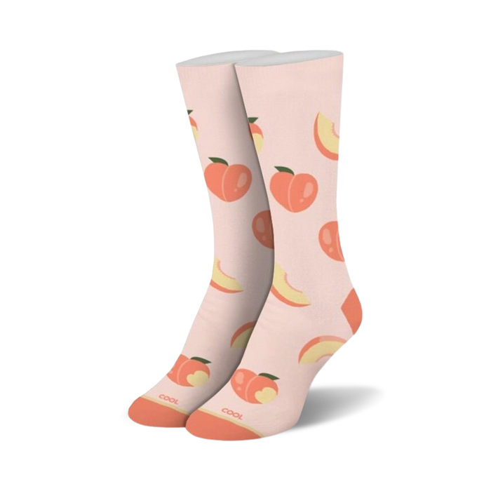 A pair of crew socks standing upright, light peach with an all-over pattern of whole peaches and peach slices, orange toes and heels.