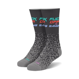 Pair of crew socks in dark gray with 'Fuck Off I'm Gaming' text in teal, pink, and red. Pixelated design fades down the sock.