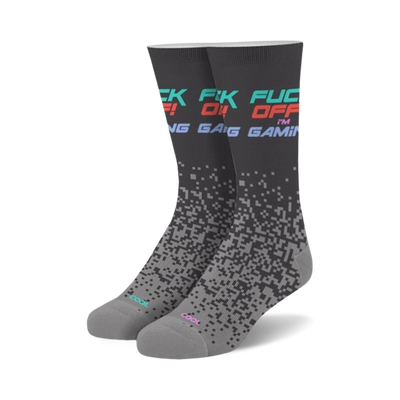 Pair of crew socks in dark gray with 'Fuck Off I'm Gaming' text in teal, pink, and red. Pixelated design fades down the sock.