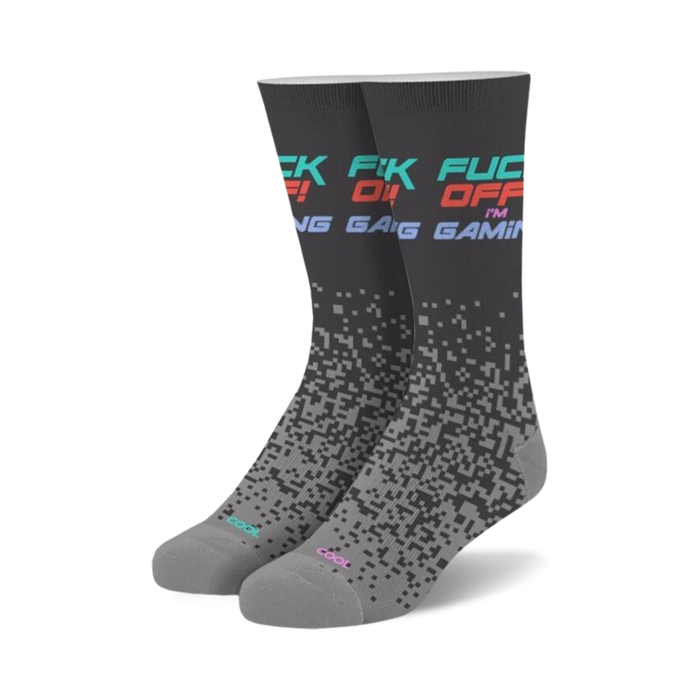Pair of crew socks in dark gray with 'Fuck Off I'm Gaming' text in teal, pink, and red. Pixelated design fades down the sock.