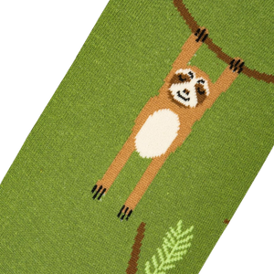A green sock with a brown sloth hanging from a branch. The sloth has a cream-colored belly and brown arms and legs. The branch is dark brown and the leaves are dark green.