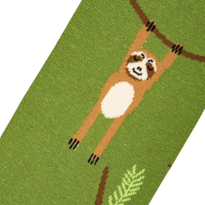 A green sock with a brown sloth hanging from a branch. The sloth has a cream-colored belly and brown arms and legs. The branch is dark brown and the leaves are dark green.