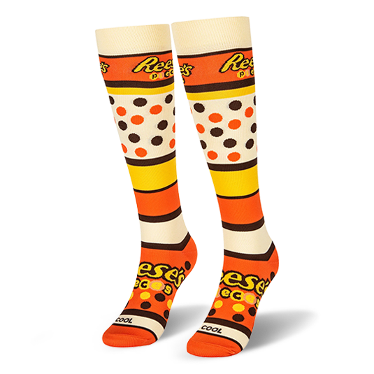 Pair of knee-high socks showing the Reese's Pieces logo, bold colored stripes, candy dots, and an orange toe box.