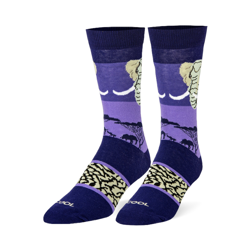 Dark blue and purple crew socks featuring an elephant head, black savanna silhouettes, and a beige wrinkled skin pattern.