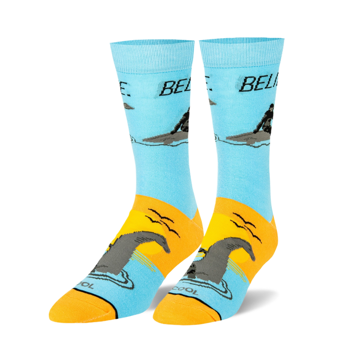 Pair of crew socks, light blue and orange, featuring a graphic of a man riding a Loch Ness Monster and the word 'BELIEVE'.
