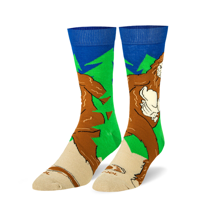 Pair of crew socks featuring a Sasquatch design.  Colors include brown, green, and blue. The Bigfoot image is walking through a forest.