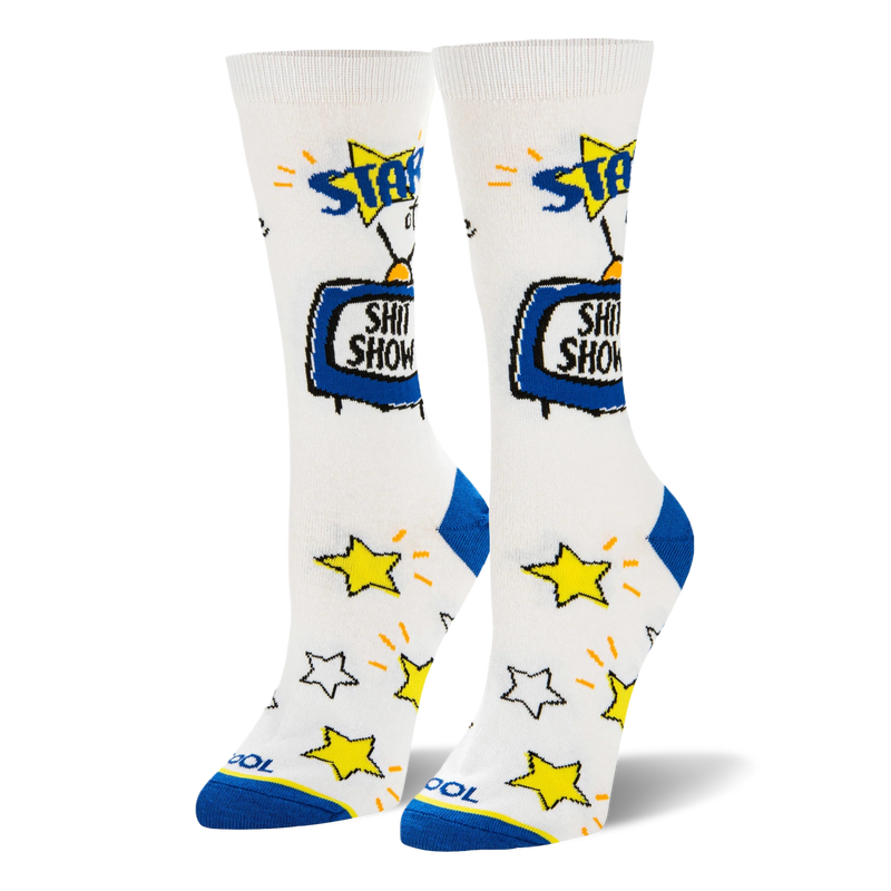 White crew socks featuring a blue retro TV that says SHIT SHOW and scattered yellow stars over the foot. Has blue heels.