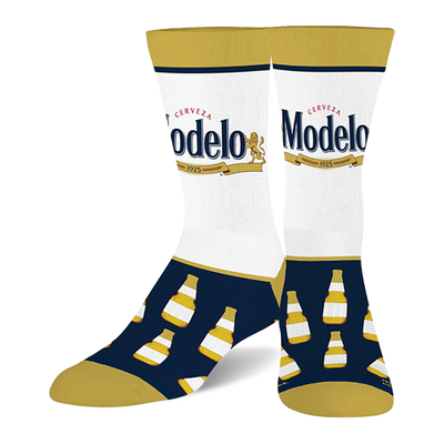 Two crew socks with white calves featuring the Modelo beer logo, navy blue feet with yellow-capped beer bottles, and gold toes, heels, and cuffs.