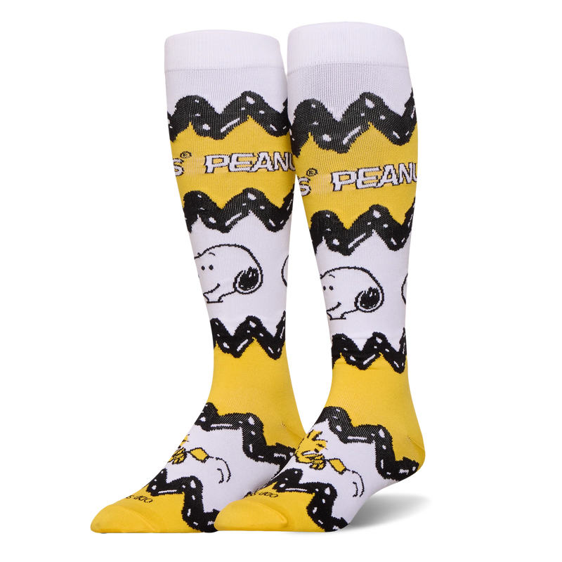 Tall yellow and white Peanuts socks featuring Charlie Brown's black zigzag pattern, Snoopy's face, and Woodstock at the toe.