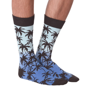 A person is modeling a pair of orange and black palm tree socks. The socks are folded over showing the 
