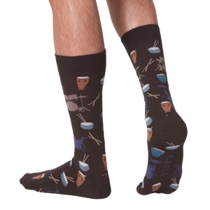 Lifestyle shot showing the 'Drums' socks on a person's legs from the back. The socks are dark brown with a drum set pattern.