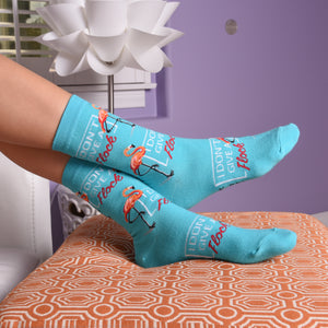 A pair of teal socks with a flamingo design. The flamingo is standing on one leg and has the words 