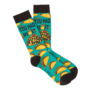 Pair of teal crew socks with a repeating pattern of tacos and the phrase 'You Had Me at Tacos.'  Black cuff.