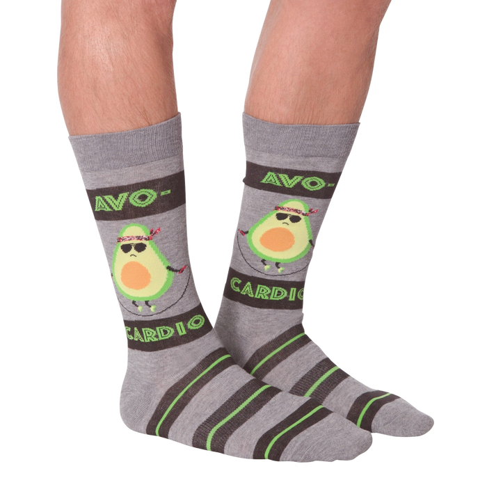 A pair of gray socks with green and brown stripes at the top. The socks have a pattern of avocados wearing sunglasses and jumping rope. The text 